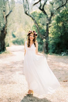 Bride stands in a white toga dress holding the hem with her hand in the park. High quality photo