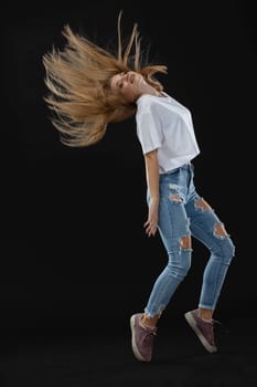 Dance pose in motion. A teenage dancer throws her hair up while standing bent back on her toes. She looks into the camera. Young professional dancer.