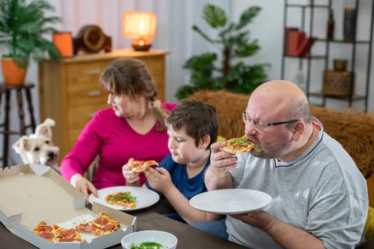 A shaggy dog demands another slice of pizza from a consuming family. Father, son and mother all eat the thin crust pizza.