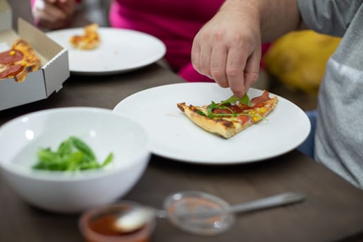 The man adds green arugula to the pizza to enhance and diversify the flavor of each bite.