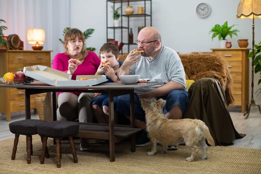 A shaggy dog watches when he too gets his slice. Mother, Father and son help themselves to hot and fragrant slices of pizza from a box.