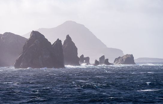 Jagged rocky outcroppings off Hornos Island with Cape Horn in distance