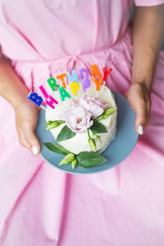 happy birthday cake with letters happy birthday in the form of candles, a very colorful and very tasty girl in a pink dress holds in her hands. Holiday and surprise concept