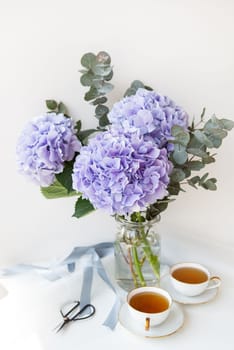 Two cups of black tea in a porcelain beautiful white cup with a gold cut. Beautiful bouquet of purple hydrangea on the table. Tea ceremony concept