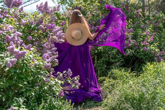 Fashion Model in Lilac Flowers, Young Woman in Beautiful Long Dress Waving on Wind, Outdoor Beauty Portrait in Blooming Garden.