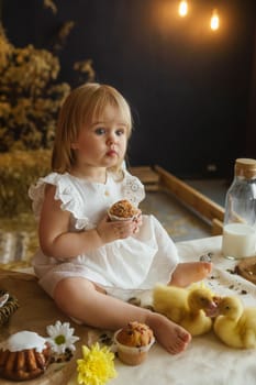 A little girl is sitting on the Easter table and playing with cute fluffy ducklings. The concept of celebrating happy Easter