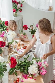 A little blonde girl with her mom on a kitchen countertop decorated with peonies. The concept of the relationship between mother and daughter. Spring atmosphere