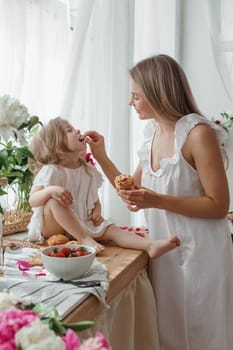 A little blonde girl with her mom on a kitchen countertop decorated with peonies. The concept of the relationship between mother and daughter. Spring atmosphere.