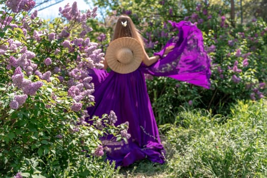 Fashion Model in Lilac Flowers, Young Woman in Beautiful Long Dress Waving on Wind, Outdoor Beauty Portrait in Blooming Garden.