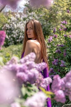 portrait of young woman with long hair outdoors in blooming lilac garden.