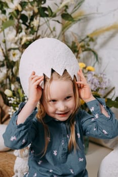 Girl in a beautiful Easter photo zone with flowers, eggs, chickens and Easter bunnies. Happy Easter holiday