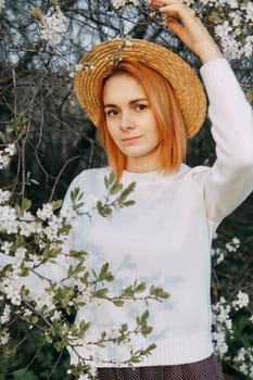 Portrait of a woman in a straw hat in a cherry blossom. Free outdoor recreation, spring blooming garden