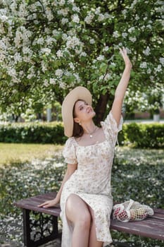 An attractive long-haired woman walks in the spring in the park of blooming apple trees. Spring portrait of a woman