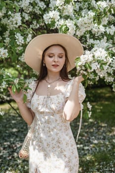 An attractive long-haired woman walks in the spring in the park of blooming apple trees. Spring portrait of a woman