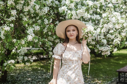 An attractive long-haired woman walks in the spring in the park of blooming apple trees. Spring portrait of a woman