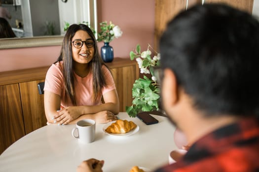 Young diverse loving couple eating croissant and talks together at home in breakfast time. Communication and relationship