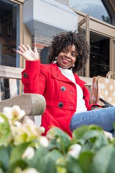 portrait of a beautiful african american woman sitting on a park bench and waving to someone in the distance while waiting for her friend. High quality photo