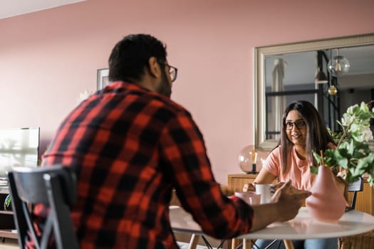 Young diverse loving couple eating croissant and talks together at home in breakfast time. Communication and relationship