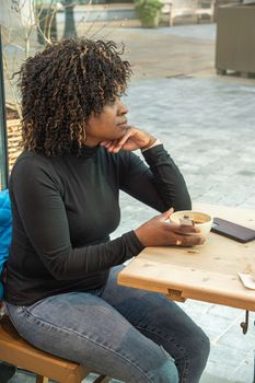 pensive african american woman sitting in a cafe and looking out the window with a cup of hot, coffee or resting from household chores alone, High quality photo
