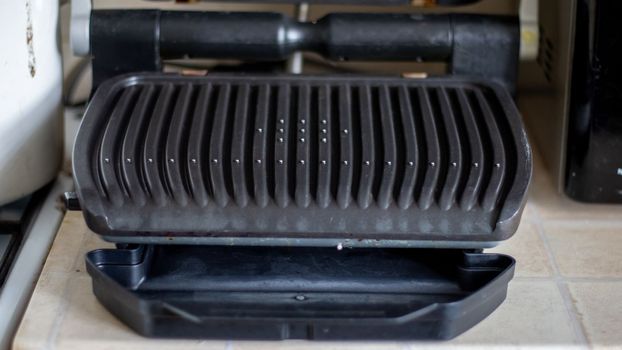 Black electric grill grate, textured background. The surface of the electric grill. Pollution of the surface of the electric stove. Close-up of a home electric grill, in the kitchen. BBQ