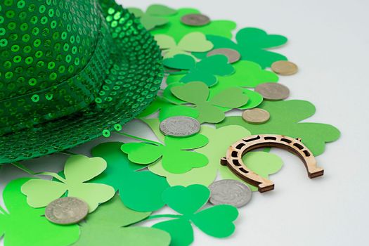 St. Patrick's Day concept. Mock-up, layout of green clover, shamrock on white background and green top hat with wooden horseshoe and metal coins Close-up. Soft focus. Irish holiday.