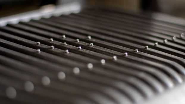 Black electric grill grate, textured background. The surface of the electric grill. Pollution of the surface of the electric stove. Close-up of a home electric grill, in the kitchen. BBQ