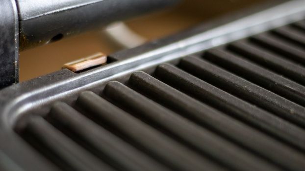 Black electric grill grate, textured background. The surface of the electric grill. Pollution of the surface of the electric stove. Close-up of a home electric grill, in the kitchen. BBQ