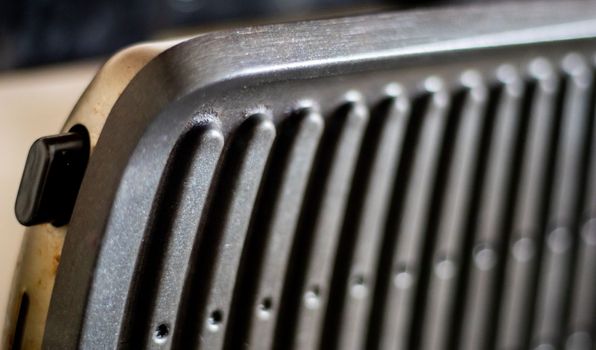 Black electric grill grate, textured background. The surface of the electric grill. Pollution of the surface of the electric stove. Close-up of a home electric grill, in the kitchen. BBQ