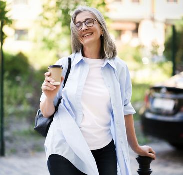 Happy mature woman enjoying a cup of coffee on a summer day while sitting outdoors on a city street. She appears content and relaxed, savoring the simple pleasures of life. High quality photo