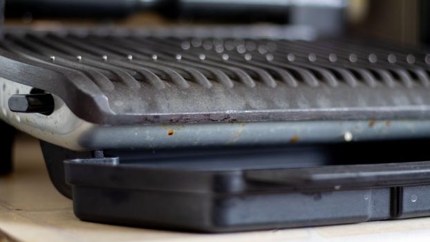 Black electric grill grate, textured background. The surface of the electric grill. Pollution of the surface of the electric stove. Close-up of a home electric grill, in the kitchen. BBQ