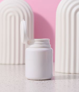 White plastic jar with an open lid for cosmetics and medical preparations on a pink background