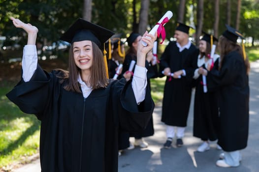 Group of happy students in graduation gowns outdoors. A young girl boasts of her diploma