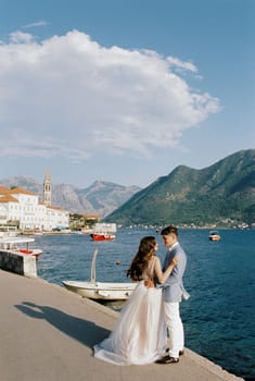 Bride and groom are standing on the Perast pier near the moored boats. High quality photo