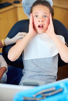 How many cavities. a young girl looking terrified while sitting in a dentists chair