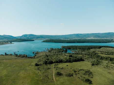 Aerial landscape from flying drone storage reservoir at mountain foot covered colorful spring forest. Beautiful view from above blue lake among highlands