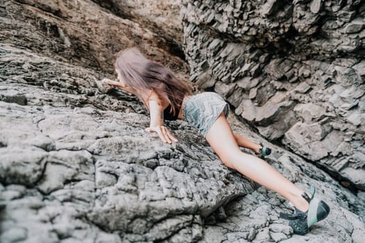 A girl climbs a rock. The athlete trains in nature. Woman overcomes difficult climbing route. Extreme hobby. Tourist woman rock climber hiking on mountains rocks over beautiful sea coast