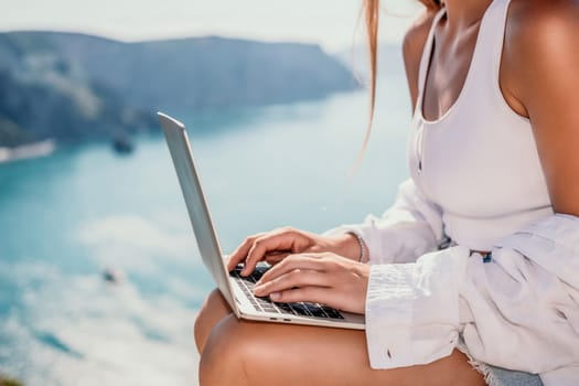 Digital nomad, Business woman working on laptop by the sea. Pretty lady typing on computer by the sea at sunset, makes a business transaction online from a distance. Freelance remote work on vacation