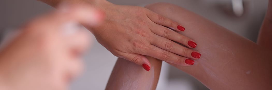 Mom applies sunscreen spray on daughter legs closeup. Red baby skin and sunburn concept