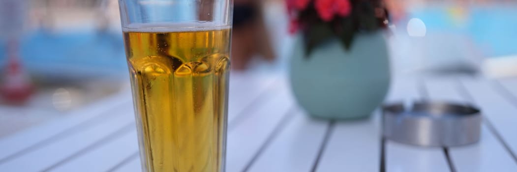 One cold alcoholic beer in transparent glass on sunny day by pool. Cold beer and tea in summer heat