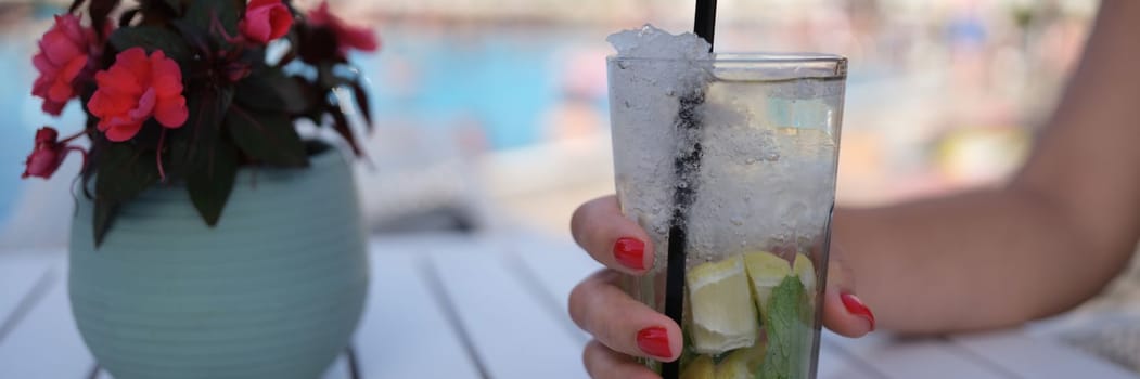 Beautiful glass with refreshing cocktail in woman hand on background of pool. Summer cold drinks concept