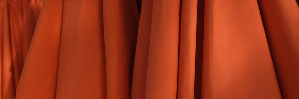 Red orange umbrellas stand stacked on beach. Sun protection equipment for beach