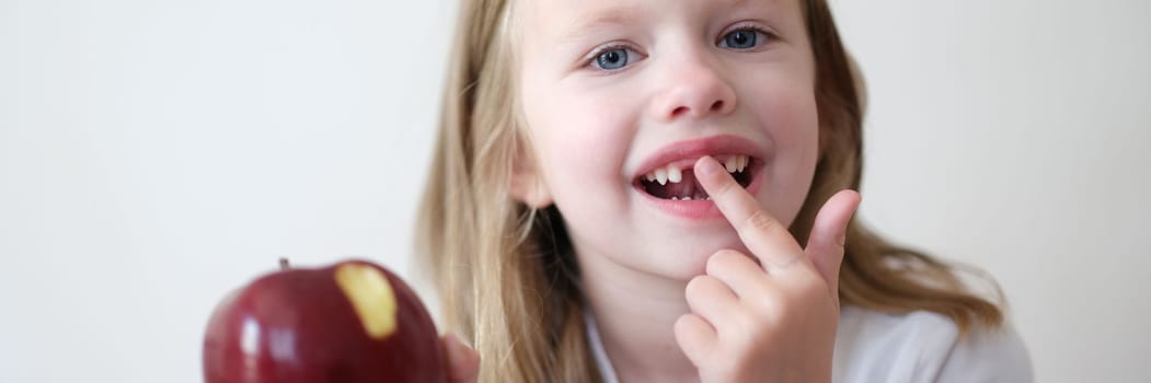 Portrait of smiling cute girl without teeth with red bitten apple in hand. Healthy baby teeth concept