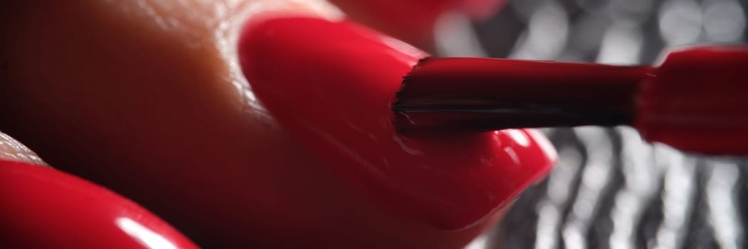 Master manicurist applies decorative bright red varnish on nail plate with brush. Concept of beauty and nail care