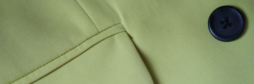 Closeup of green jacket with black button and pocket. Details of stylish green jacket