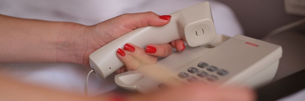 Woman picks up phone and dials number for room service in hotel closeup. Hotel service and call to reception concept