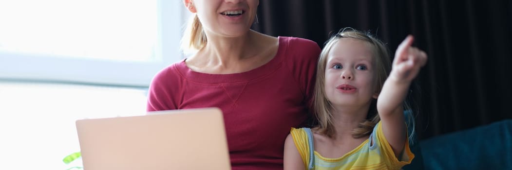 Portrait of mother and child sitting on sofa with laptop looking away in surprise. Emotions of surprise and delight