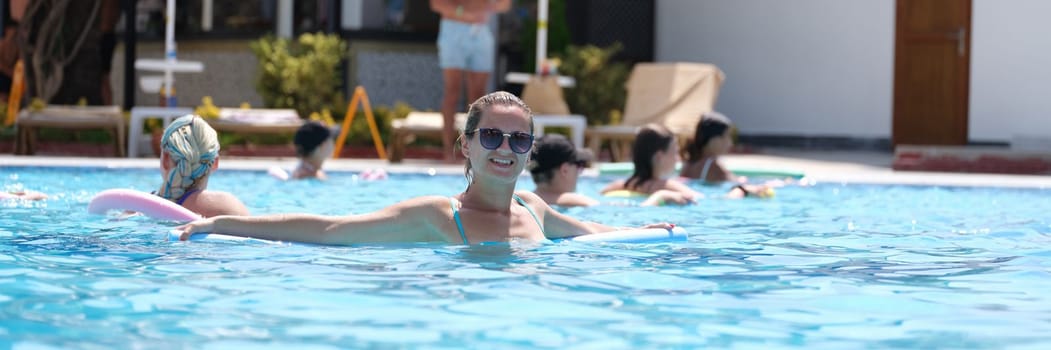 Young woman in sunglasses swims with aqua noodles in pool. Aqua aerobics concept