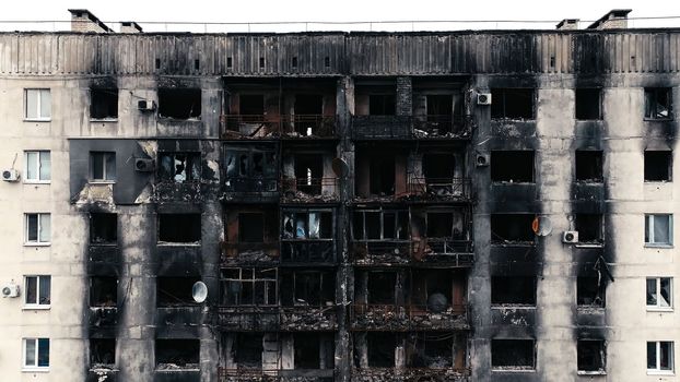 A burnt-out high-rise in the war zone. Damage to a residential building as a result of artillery shelling. War in residential areas, broken windows and burned apartments. Armed conflict in Ukraine.