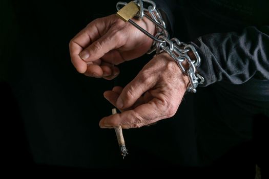 man smoking with chained hands on black background, concept of addiction