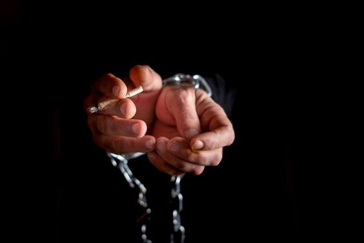man's hands chained, with a cigarette in his fingers black background, addiction concept